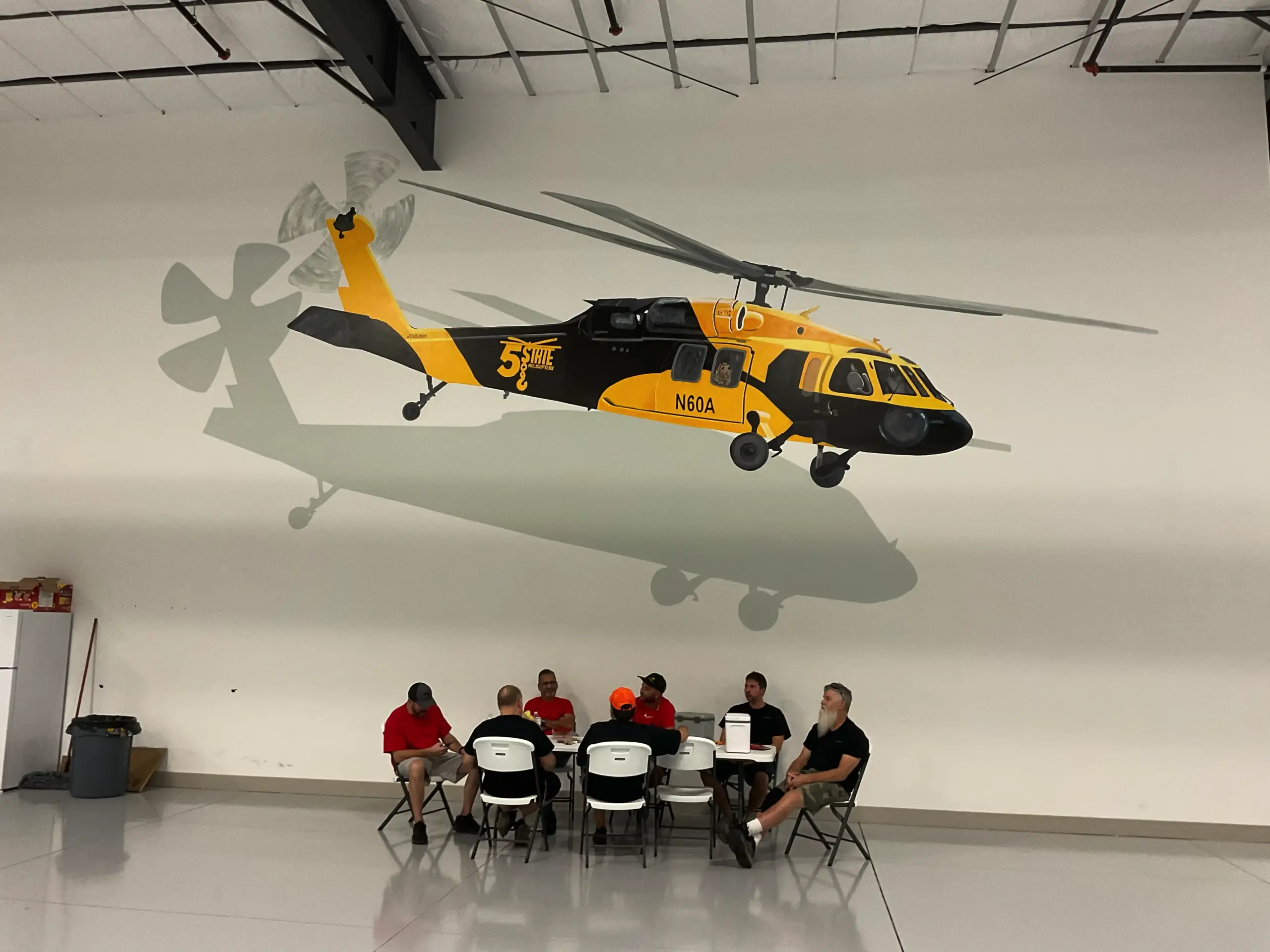 People sit beneath large helicopter mural indoors