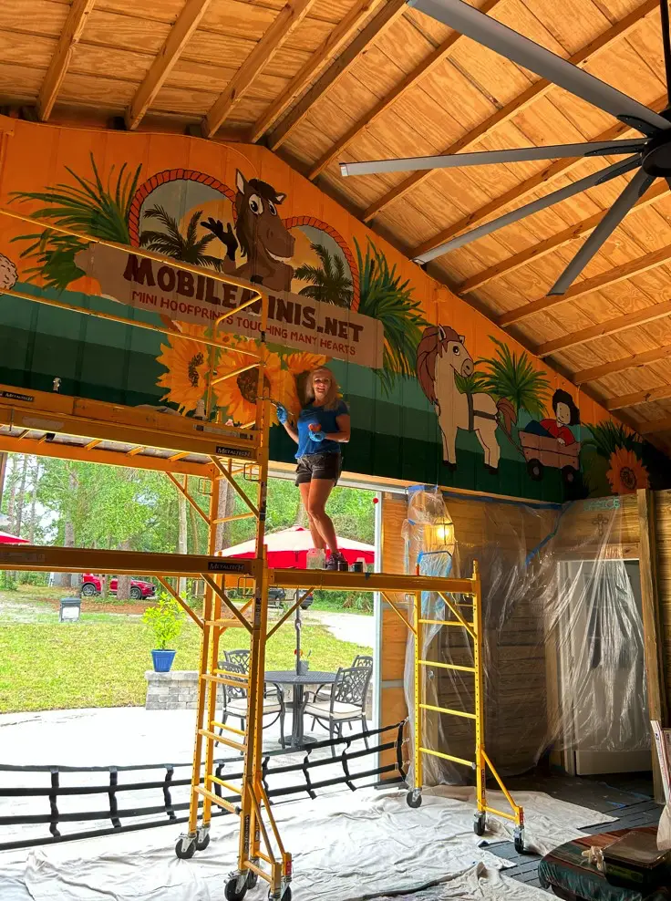 Artist painting barn mural with cartoon horses.