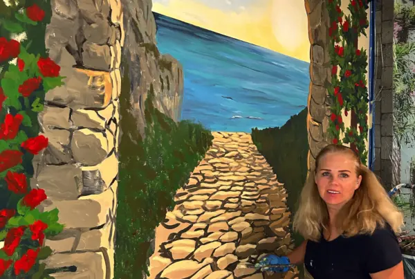 Artist painting seaside archway mural with stones and roses