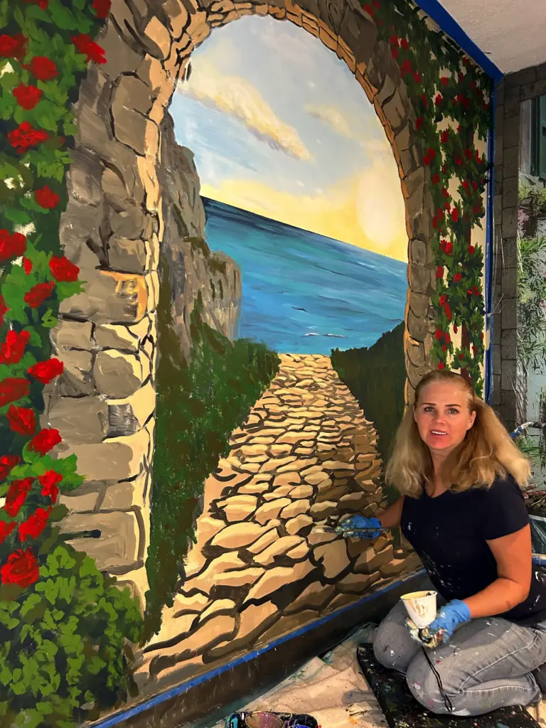 Artist painting seaside archway mural with stones and roses