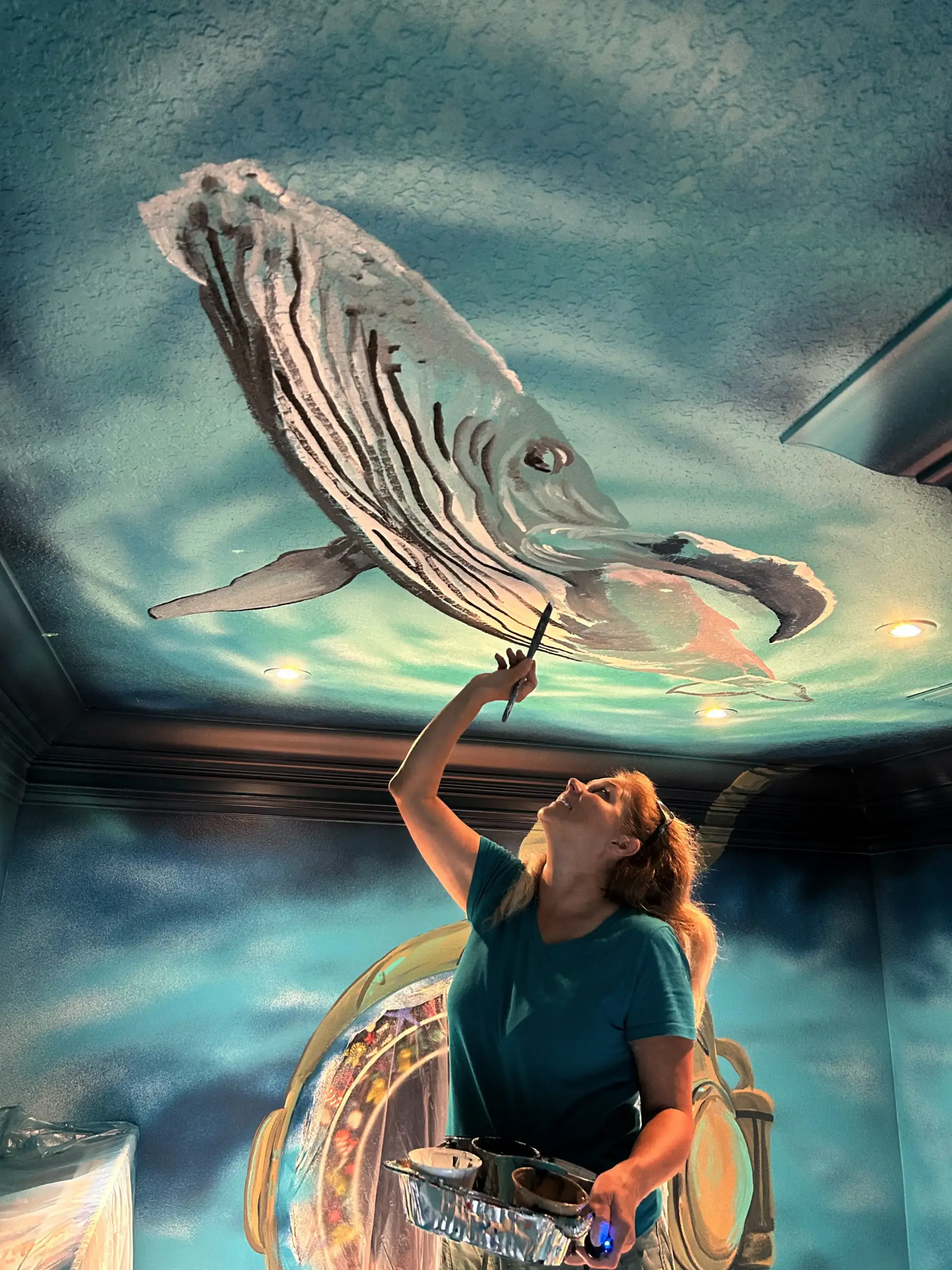 Artist painting whale mural on ceiling