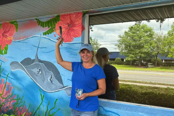 Woman painting ocean mural on building wall