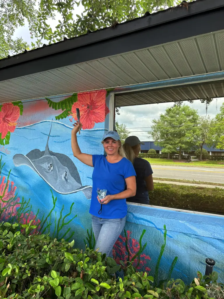 Woman painting ocean mural on building wall