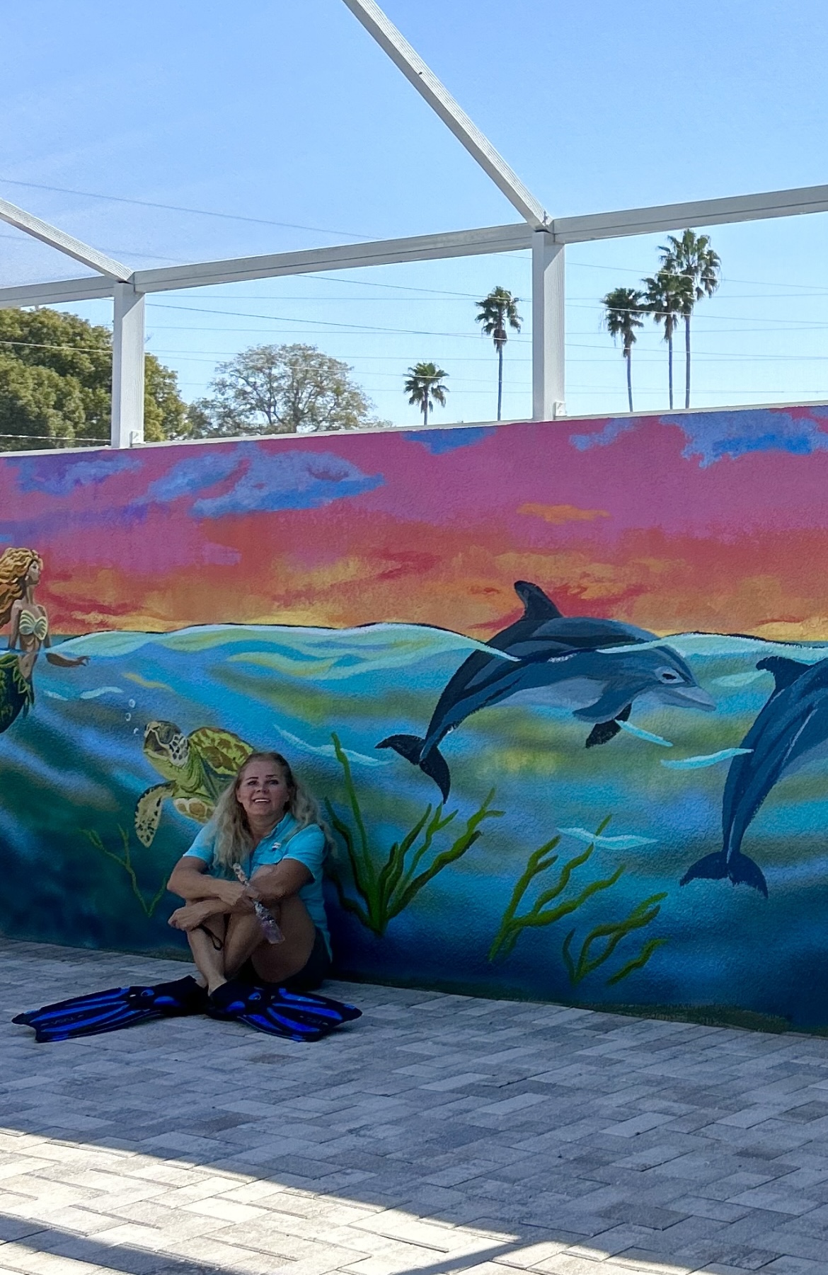 Woman sitting by colorful ocean mural with dolphins.