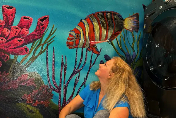 Woman sitting by colorful underwater mural.