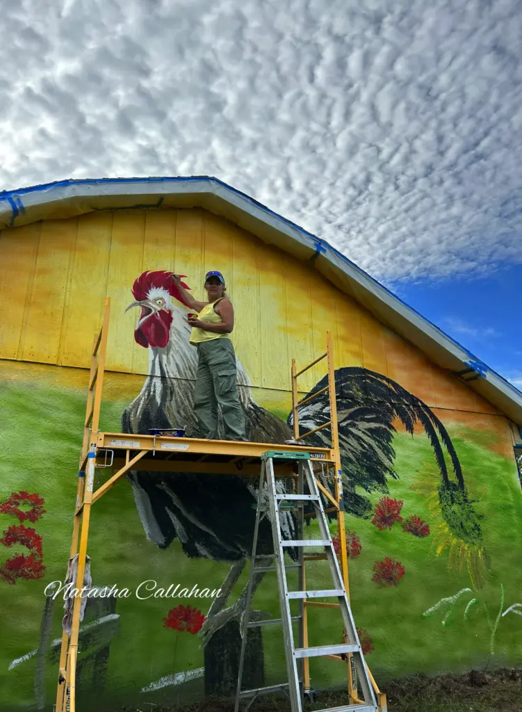 Artist painting colorful rooster mural on barn
