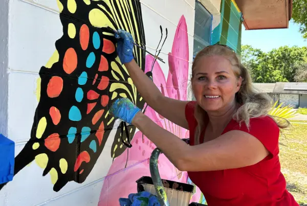 Woman painting colorful butterfly mural on wall