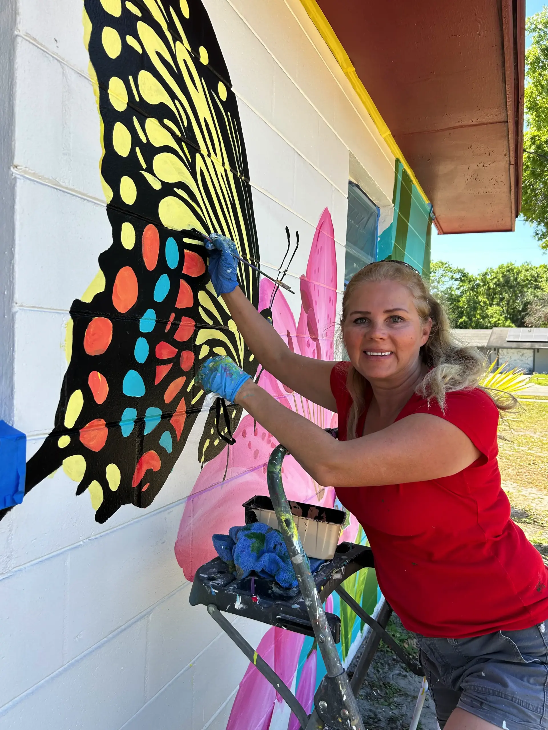 Woman painting colorful butterfly mural on wall
