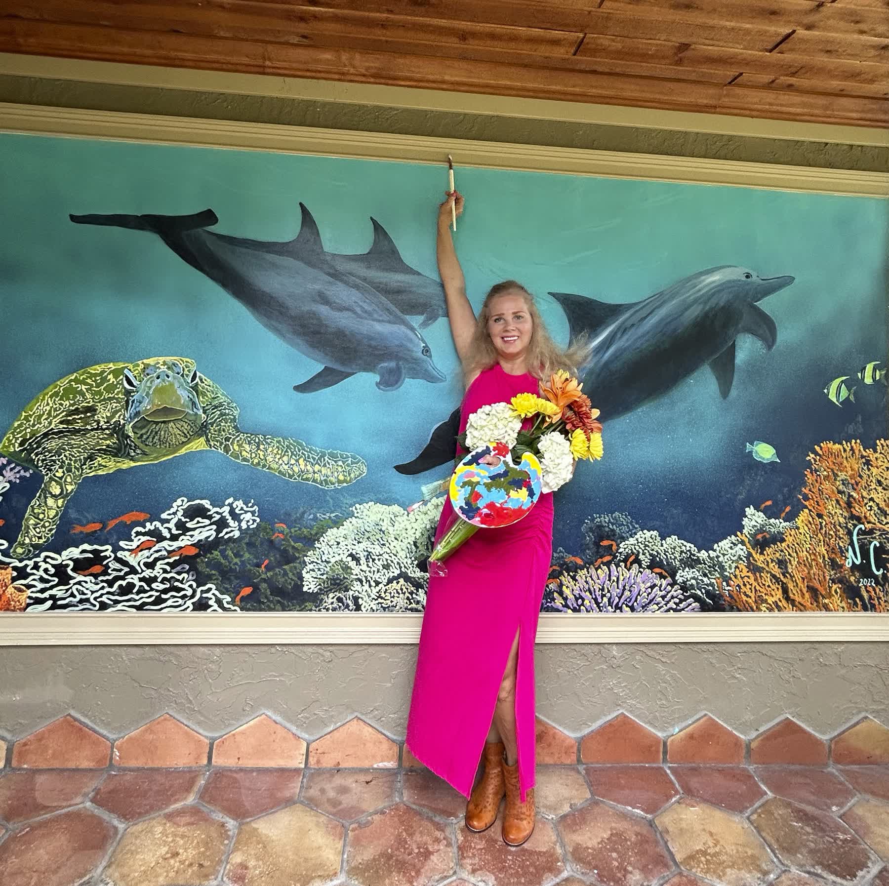 Artist posing with ocean mural and flowers